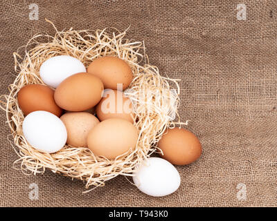 Assorted chicken, hens eggs in basket with straw on hessian rustic background with copy space. Different colors: brown white and speckled. Stock Photo