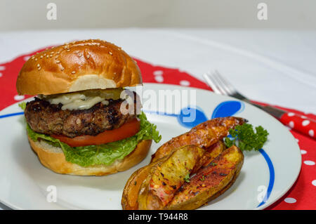 Cooked, homemade 50/50 burger served with potato wedges and vegetable toppings. Concept for summer, barbecue, restaurant, menus, food blog, comfort fo Stock Photo