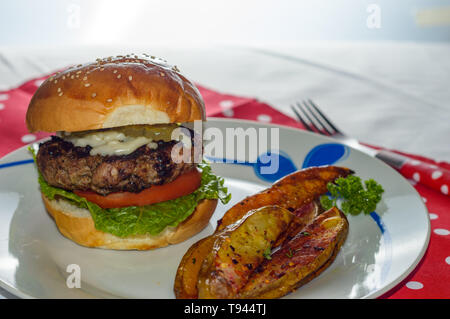 Cooked, homemade burger served with potato wedges and vegetable toppings. Concept for summer, barbecue, restaurant, menus, food blog, comfort food, Am Stock Photo