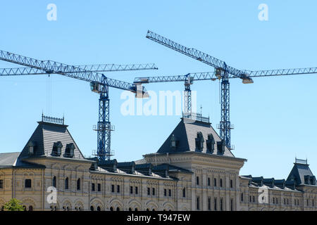 Several working tower cranes over the roof of a Gothic building against a blue sky Stock Photo