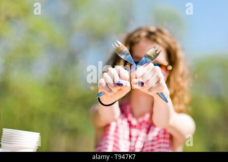 Teen aged girl in red checkered shirt sitting by table on birthday garden party - crossing forks Stock Photo