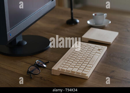 Modena, Italy, 04/07/2018 : Office table desk. Workspace with large black monitor screen, a wooden keyboard, a trackpad, a graphic pen, glasses, a cof Stock Photo