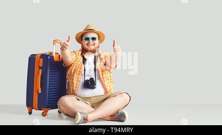 Fat funny man with a suitcase smiling on a gray background. Stock Photo