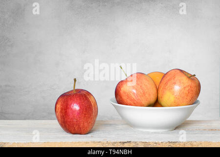 Some red apples on a white wooden shelf and a bowl against a white background. Empty copy space for Editor's text. Stock Photo