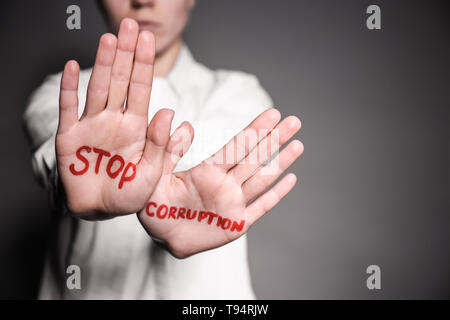 Woman with text STOP CORRUPTION written on her palms against grey background, closeup Stock Photo