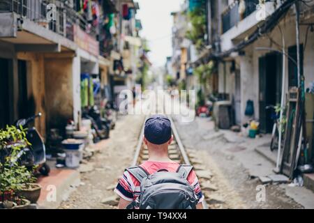 Man with backpack walking in narrow Hanoi Train Street, Vietnam. Stock Photo