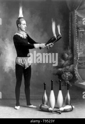 Entitled: 'J.T. Doyle holding 2 burning juggling clubs'. Juggling is a physical skill, performed by a juggler, involving the manipulation of objects for recreation, entertainment, art or sport. The most recognizable form of juggling is toss juggling. Juggling can be the manipulation of one object or many objects at the same time, using one or many hands. Jugglers often refer to the objects they juggle as props. The most common props are balls, clubs, or rings. Some jugglers use more dramatic objects such as knives, fire torches or chainsaws. Photographed by J.E. Pasonault, 1902. Stock Photo