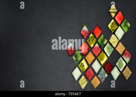 Abstract composition of diamond shape various fruit puzzle on black stone background with copy space Stock Photo