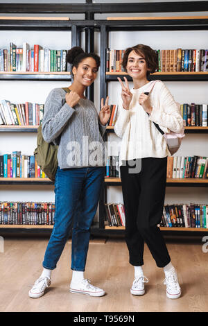 Two cheerful young girls students studying at library, carrying backpacks Stock Photo