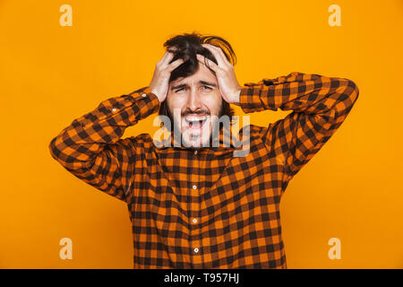 Portrait of uptight man grabbing head and shouting while standing isolated over yellow background in studio Stock Photo