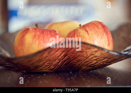Red fresh three apples in dark brown plate on glossy dark table. Sweet and fresh apples on dark plate with light bokeh background. Stock Photo