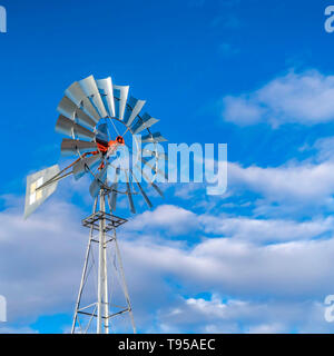 Clear Square Shiny steel windpump against a vibrant blue sky with cottony clouds Stock Photo