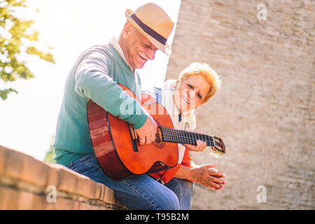 Happy senior couple playing a guitar and having a romantic date outdoor - Mature people having fun enjoying time together in vacation Stock Photo