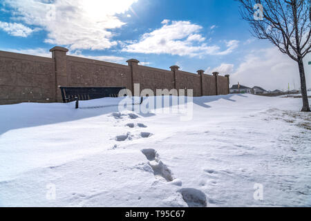 Footprints leading to an empty bench with the seat buried in snow during winter Stock Photo