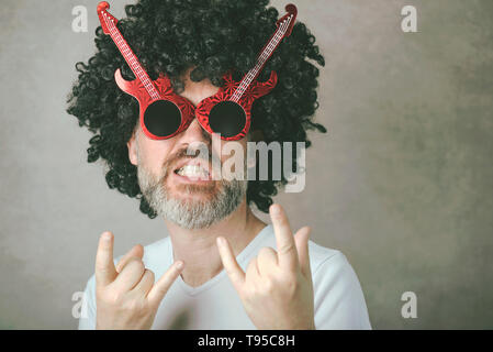 funny mature man with sunglasses doing rock symbol with hands up against gray background Stock Photo