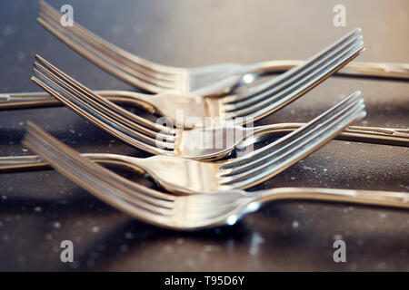 Crossed five steel forks on black table. Macro photography for dishware design and kitchen theme. Stock Photo