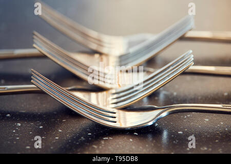 Crossed five steel forks on black table. Macro photography for dishware design and kitchen theme. Stock Photo