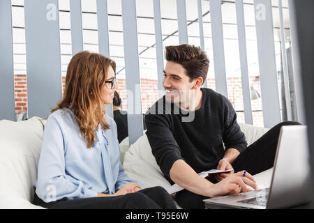 Cheerful young couple of colleagues working together at the office, co-working teamwork concept, using laptop Stock Photo