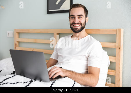 Handsome young man laying in bed, working on laptop computer Stock Photo
