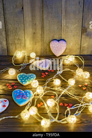 Garlands and ginger multi-colored traditional gingerbread hearts on wooden background, festive concept. Stock Photo