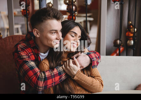 Picture of a cute young happy loving couple sitting in cafe indoors hugging. Stock Photo