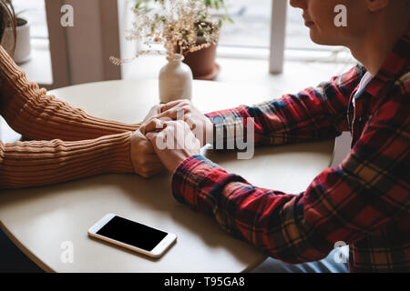 Cropped picture of a cute young loving couple sitting in cafe indoors holding hands of each other. Stock Photo