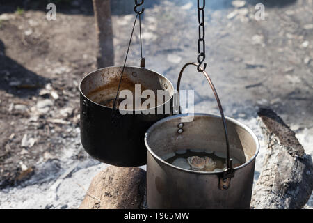 Cooking in two sooty old cauldrons on campfire at forest Stock Photo