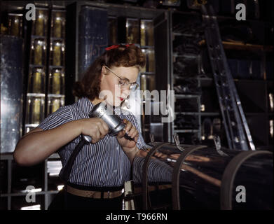 Operating a hand drill at the North American Aviation, Inc., a woman is in the control surface department assembling a section of the leading edge for the horizontal stabilizer of a plane. Although the image of 'Rosie the Riveter' reflected the industrial work of welders and riveters, the majority of working women filled non-factory positions in every sector of the economy. What unified the experiences of these women was that they proved to themselves, and the country, that they could do a man's job  and could do it well. Photographed by Alfred T. Palmer, 1942. Stock Photo
