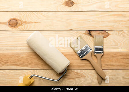 paint roller and two brushes on wooden surface
