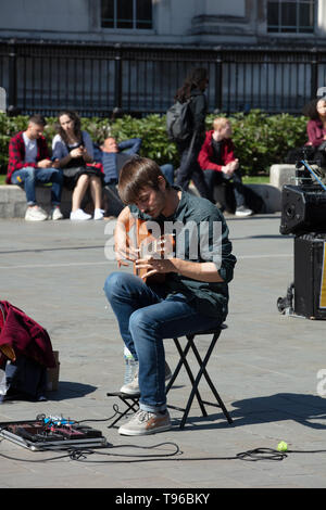 Street performer plays the classical guitar music on Trafalgar Square London, UK on a warm and sunny day in May entertaining tourists and Londoners. Stock Photo
