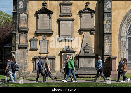 Trourists on a walking tour stroll by memorials on the wall of Greyfriars Kirk in Edinburgh, Scotland, UK. Stock Photo