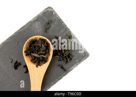 Small pieces of dried Wakame (Undaria pinnatifida), edible seaweed, ingredient to different foods in wooden spoon on black stone cutting board isolate Stock Photo