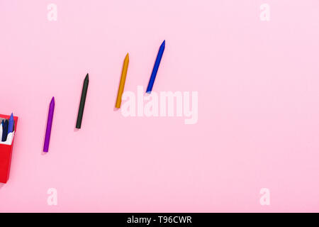 top view of colorful crayons in row and cigarette pack on pink with copy space, smoking concept