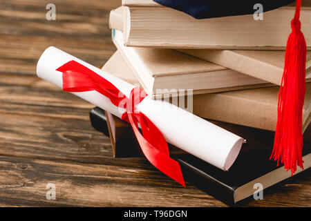 diploma with ribbon and stack of books on wooden surface Stock Photo