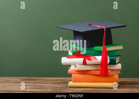 books, diploma with ribbon and academic cap on wooden surface isolated on green Stock Photo