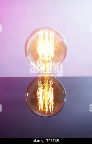 Glowing retro light bulb with reflection on color background Stock Photo