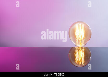 Glowing retro light bulb with reflection on color background Stock Photo