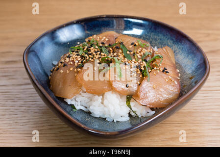 bowl with salmon sashimi seasoned with black and white sesame, rocket, nori seaweed fried on a bed of steamed white rice, wooden table background Stock Photo