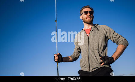 Man dressed in casual wear and sunglasses on a yacht. Happy adult bearded yachtsman close-up portrait. Handsome sailor on a boat smiling during regata Stock Photo