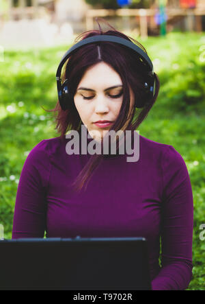 Beautiful young pretty woman in park outdoors using laptop computer listening music. Stock Photo