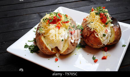 Close up of a hot baked potato topped with sour cream, green onions and cheese on black wooden board Stock Photo