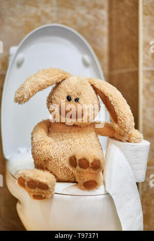 Soft stuffed rabbit with toilet paper in the toilet. The concept of digestive problems. Stock Photo