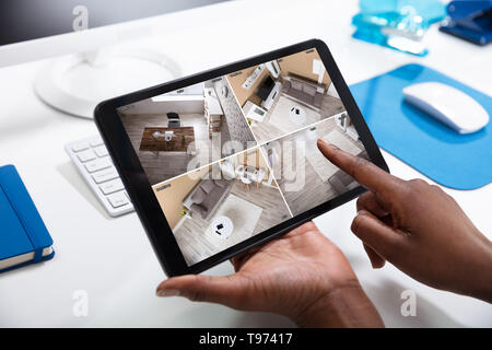 Close-up Of Person's Hand Monitoring CCTV Footage On Digital Tablet Stock Photo