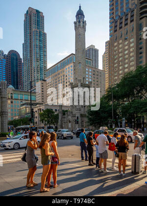 Afternoon sun shines on passersby beside the Chicago Water Tower at 806 North Michigan Avenue along the Magnificent Mile shopping district in the Near North Side community area of Chicago, IL. The tower was constructed to house a large water pump, intended to draw water from Lake Michigan. Built in 1869, it is the second-oldest water tower in the United States. Stock Photo