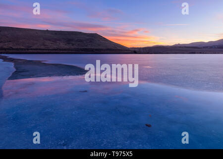 Sunset Frozen Lake - A colorful sunset reflecting in a melting frozen mountain lake. Bear Creek Park, Denver-Lakewood, Colorado, USA. Stock Photo