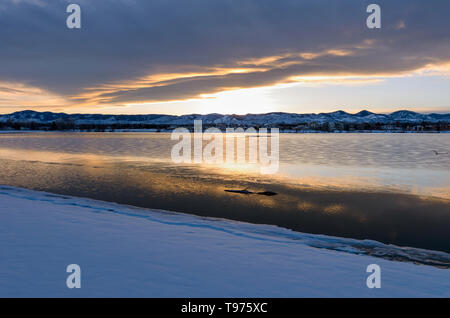 Stormy Winter Lake - A sunset view of winter storm clouds hanging over a snow and ice covered mountain city lake. Johnson Reservoir, Littleton, CO, US. Stock Photo