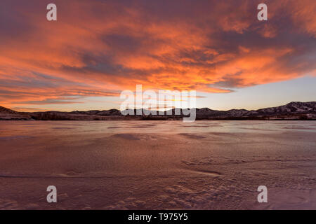 Fiery Clouds - Bright and colorful winter sunset clouds rolling over a frozen mountain lake. Bear Creek Park, Denver-Lakewood, Colorado, USA. Stock Photo