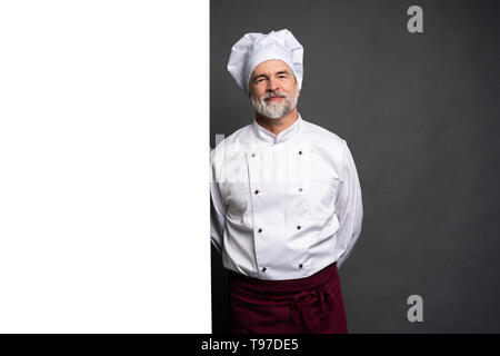 Portrait of a happy mature chef cook showing copyspace on the palms isolated on black background. Stock Photo