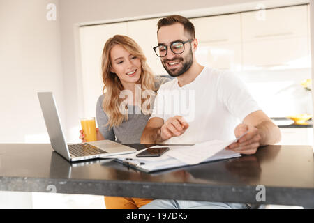 Image of amazing happy young loving couple sitting at the kitchen using laptop computer. Stock Photo