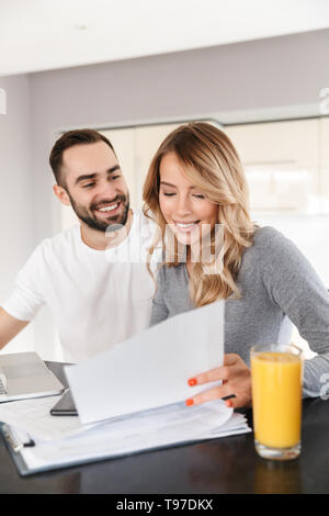 Image of young loving couple sitting at the kitchen using laptop computer and work with documents. Stock Photo